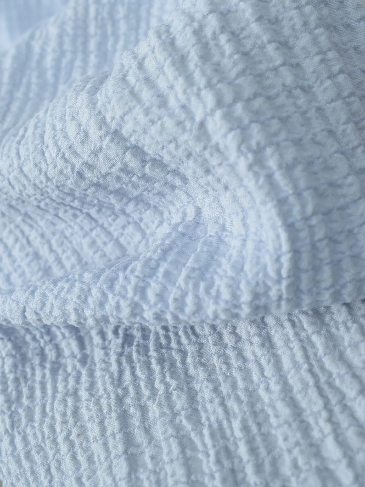 Marina pastel blue textured fabric close-up – soft crinkled breathable texture with subtle grid weave pattern and gentle drape