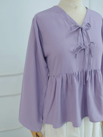 Side angle view of lilac peplum blouse showing relaxed long sleeves and gathered waist seam