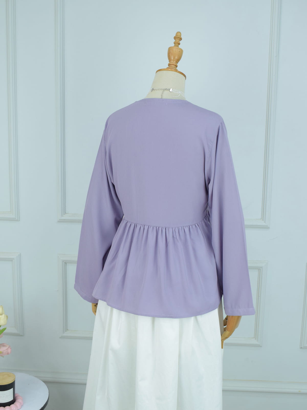 Lavender blouse on a mannequin against a light blue wall.