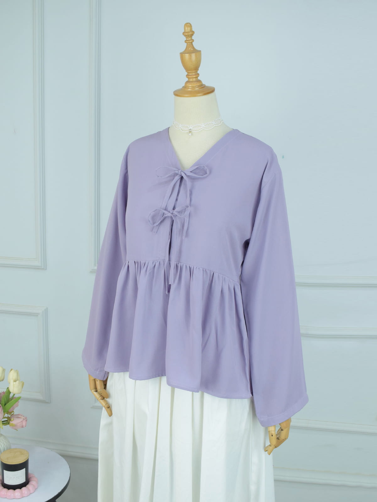 Three-quarter view of lilac long sleeve peplum top with bow ties styled over white skirt on mannequin