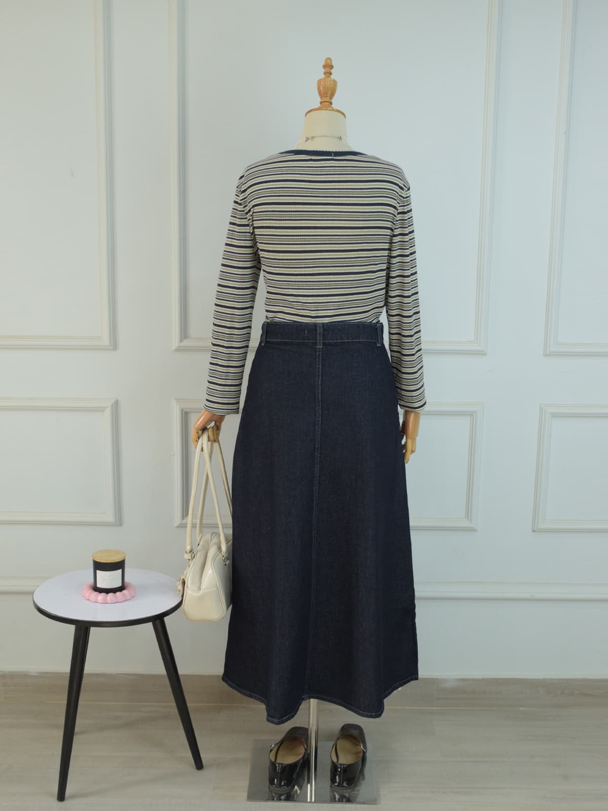 Back view of charcoal blue denim flared maxi skirt styled with striped top and white handbag on mannequin