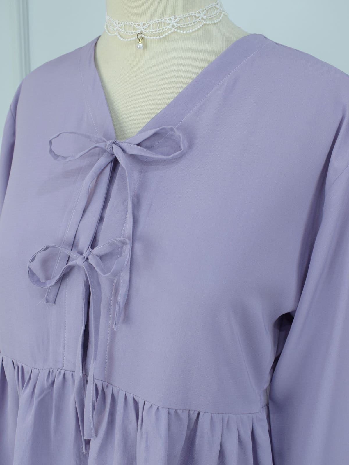 Close-up of lilac crepe peplum top showing double bow tie closures and gathered waist detail on mannequin