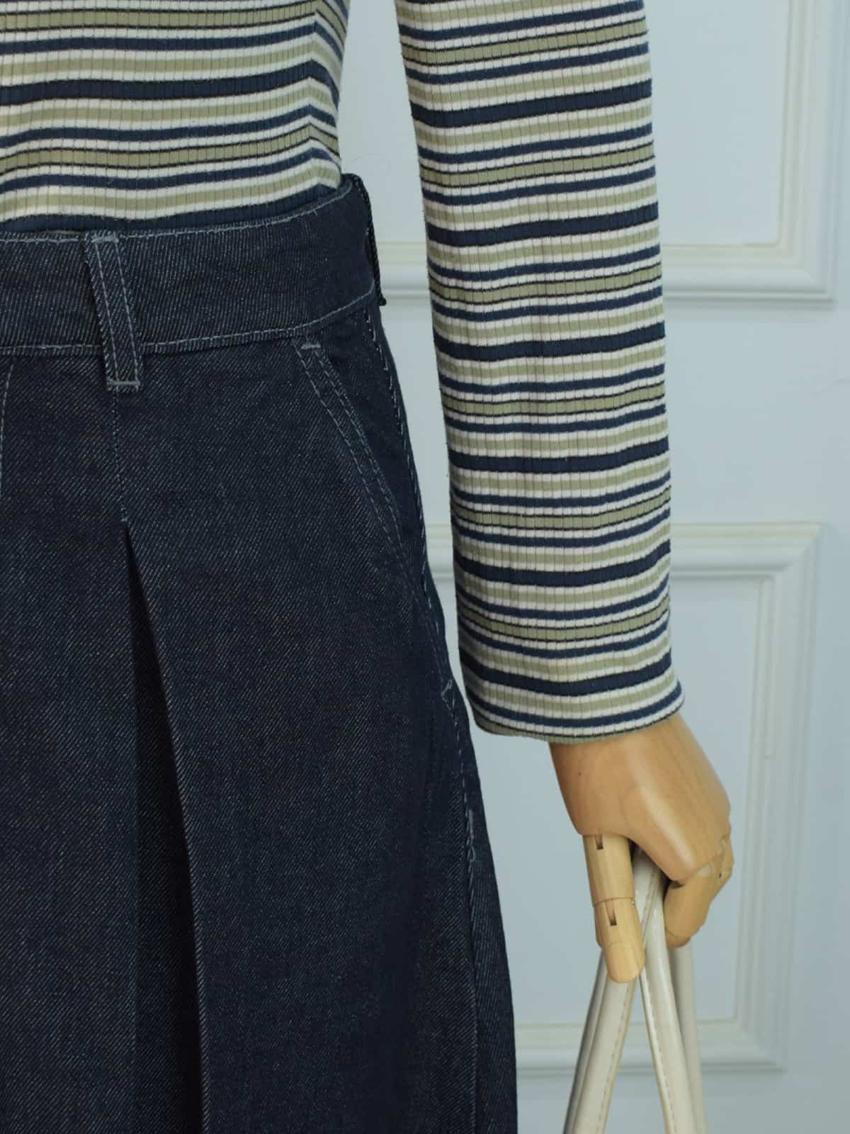 Side detail shot of dark denim skirt waistband and pleated panel flare with striped top