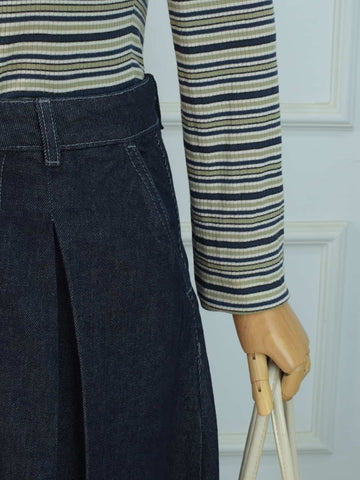 Side detail shot of dark denim skirt waistband and pleated panel flare with striped top
