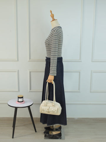 Side profile view of charcoal blue A-line denim maxi skirt styled with striped top and cream bow bag on mannequin