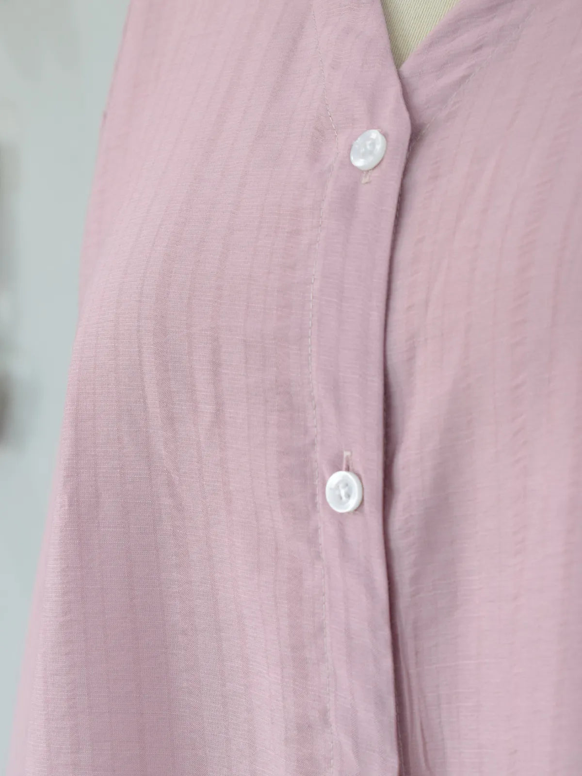 Detail shot of white pearlescent buttons on blush pink cotton striped shirt