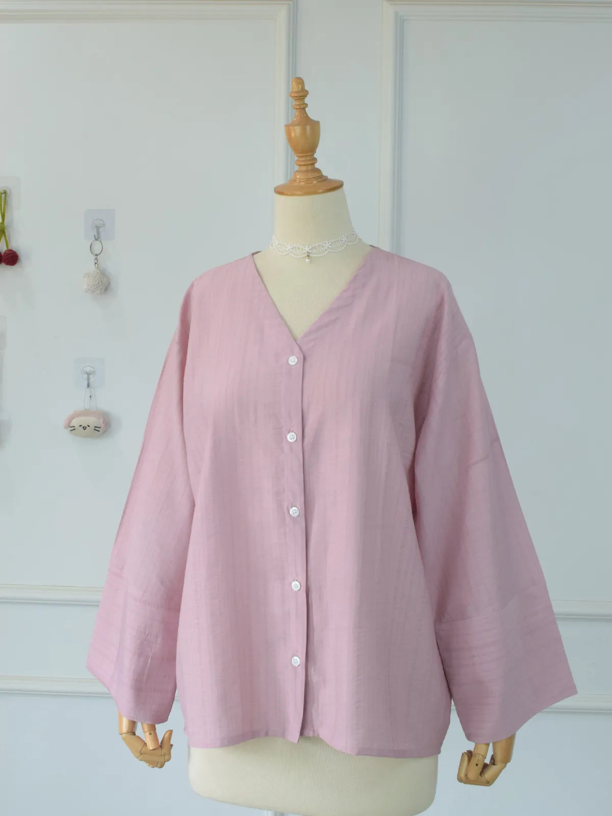 Full front view of blush pink oversized V-neck shirt with all buttons fastened on mannequin